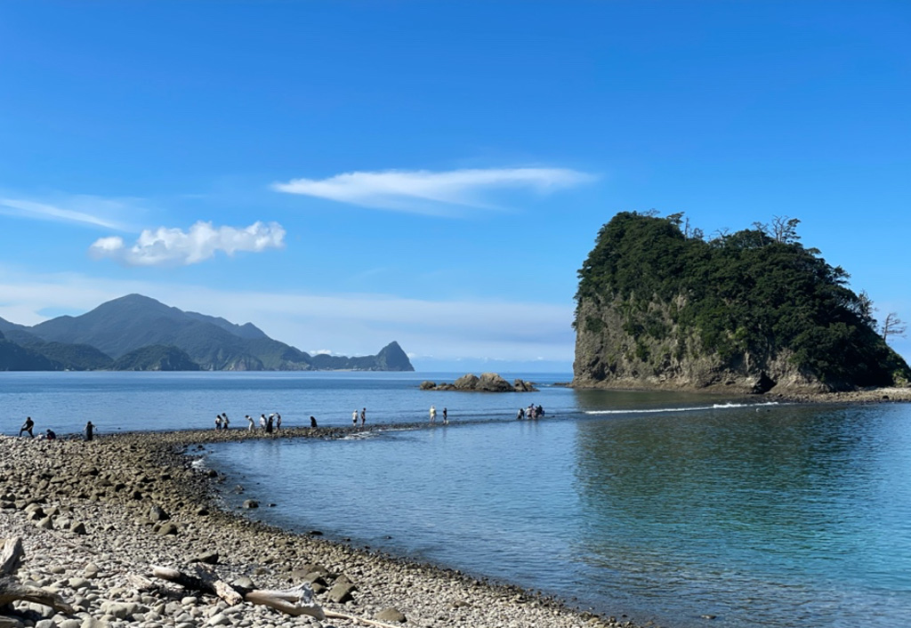 青空の下、海岸から島まで続く瀬を歩く人々